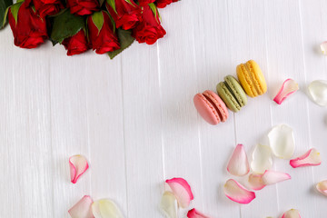 Macaroon cakes with bouquet of red roses. Different types of macaron. Colorful almond cookies. White wooden rustic background.