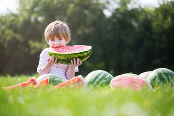 Happy smiling boy eating watermelon outdoors.