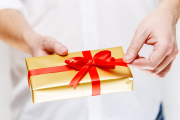 Male hands holding a gift box. Present wrapped with ribbon and bow. Christmas or birthday golden paper package. Man in white shirt.