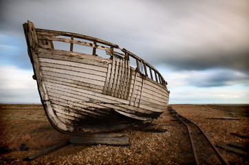 Close-up of abandoned wooden fishing boat next to old rusting rail tracks on the beach.