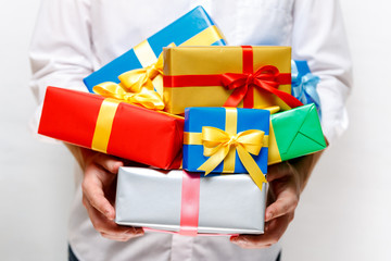 Male hands holding a gift boxes. Presents wrapped with ribbon and bow. Christmas or birthday colored packages. Man in white shirt.