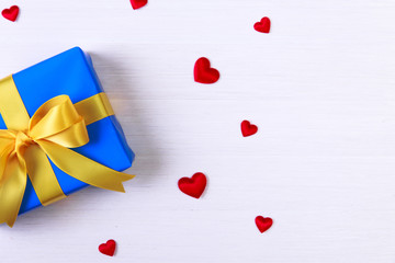 Gift box with red satin hearts. Present wrapped with yellow ribbon. Christmas or birthday blue package. On white wooden table.