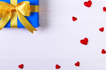 Gift box with red satin hearts. Present wrapped with yellow ribbon. Christmas or birthday blue package. On white wooden table.