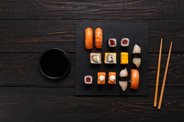 Set of salmon sushi and rolls on black wood background, top view