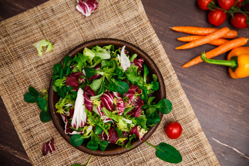 Provence salad. Leaves of endive or chicory, lamb and rose salad. Cherry tomatoes, pepper and carrot. Raw vegetables. On wooden table.