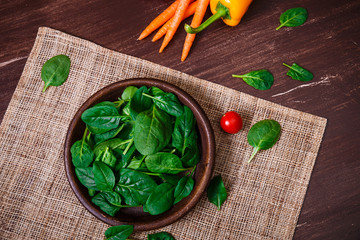 Spinach leaves in bowl. Carrot, pepper and cherry tomatoes. Raw fresh vegetable. Fresh natural plant leaf. Organic bio food on rustic wooden table.
