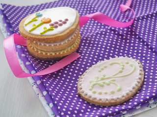 Beautiful biscuits in the shape of easter egg. Easter sugar cookies with floral ornament. Homemade cookies glazed with royal icing. Ester treat upon rustic table with pink ribbon. Selective focus.