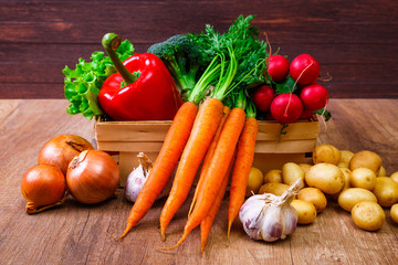 Vegetables. Potatoes, carrot and red pepper. Lettuce salad, garlic and brocoli. Onion and radish. Wooden basket on rustic table.