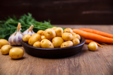 Potatoes in plate. Carrot, garlic and raw new potato. Fresh natural vegetables. Organic bio food on rustic wooden table.