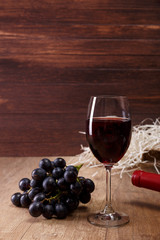 Red wine. Bottle and Wineglass with dark grapes branch. On rustic wooden background.