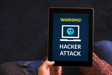 Hands holding digital tablet computer with hacker attack concept on screen. All screen content is...