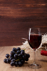 Red wine. Bottle and Wineglass with dark grapes branch. On rustic wooden background.