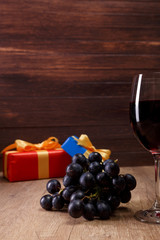 Red wine. Wineglass with dark grapes branch. Gift box with bow on rustic wooden background.