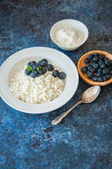 Organic Farming Cottage cheese in a white plate sour cream and blueberries on a blue stone background.