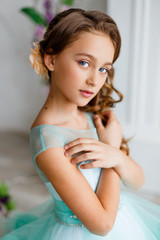 Naklejka premium portrait of a beautiful young girl with blue eyes, make up and hairstyle in a lush turquoise dress in a studio with flower decoration