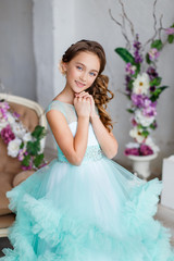 Fototapeta premium portrait of a beautiful young girl with blue eyes, make up and hairstyle in a lush turquoise dress in a studio with flower decoration