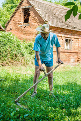 A man mows a grass with a scythe on green meadow. Summer, sunny day.