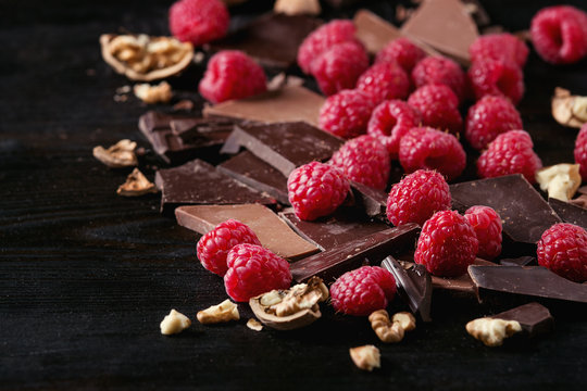 Dark and milk chopping chocolate and chips shavings chopping chocolate with fresh raspberries heap and cracks walnuts over black burnt wooden background. Close up. Chocolate dessert concept