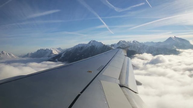 View of the Austrian Alps out of an aircraft window with the plane wing in the  foreground.
