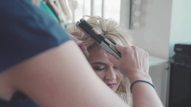 Woman in a beauty salon. Stacking. Hairdresser at work. A stylist makes a haircut (curls) for a girl. Hair stylist making ringlets to blondy woman. Fixing the Hairs.