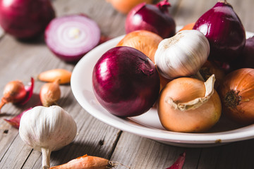 Several kinds of different onion bulbs at a white plate, standing on an old wooden table.