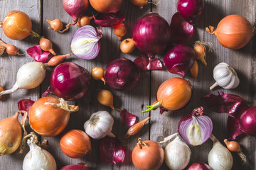 Several kinds of different onion bulbs lying on an old wooden table.