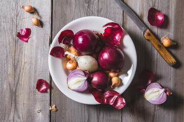 Several kinds of different onion bulbs at a white plate, standing on an old wooden table.