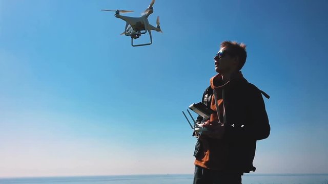 Quadrocopter drone takes off from the pilot's hand and hovers over the guy. The guy starts a drone on a green glade against the backdrop of the sea and cargo ships. Slow motion (120 fps).