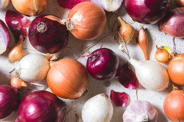 Several kinds of different onion bulbs lying on an old wooden table painted in white.