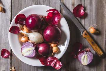 Several kinds of different onion bulbs at a white plate, standing on an old wooden table.