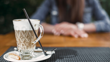 Girl with folded hands awaiting appointment. In the foreground is a sophisticated drink coffee in a transparent glass. Footage 16:9. Horizontal image.