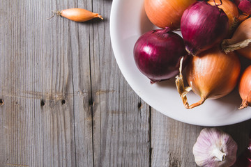Several kinds of different onion bulbs at a white plate, standing on an old wooden table.