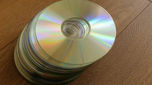 Closeup of a stack compact discs on wooden floor background. Disc falls on top.