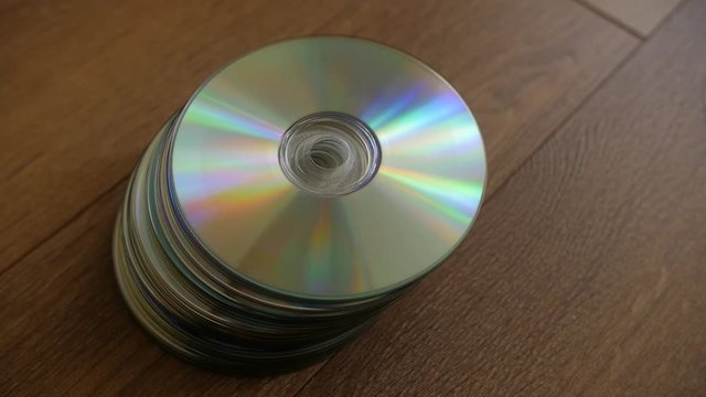 Closeup of a stack compact discs on wooden floor background. Cd falling from the top, slow-motion.