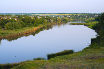 Fototapeta na wymiar Calm river flows through a village in the midst of a green prairie