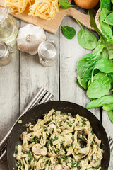 Tagliatelle pasta with spinach and mushrooms on a pan.
