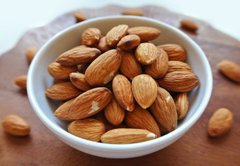 Almonds in a small white bowl on wooden table.
