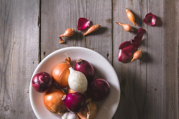 Several kinds of different onion bulbs at a white plate, standing on an old wooden table.