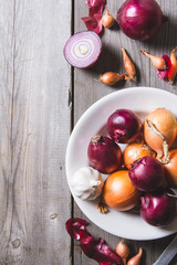 Several kinds of different onion bulbs at a white plate, standing on an old wooden table.