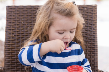 Cute baby boy eating tasty ice cream in outdoor cafe