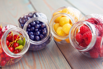 Healthy organic berry fruits in glass jar on a wooden background. Cherry, berry, blueberry, raspberry detox
