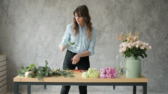 Florist at work: pretty young blond woman making fashion modern bouquet of different flowers, peone and roses