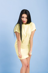 shy young brunette woman adjusts her yellow dress on blue background. 