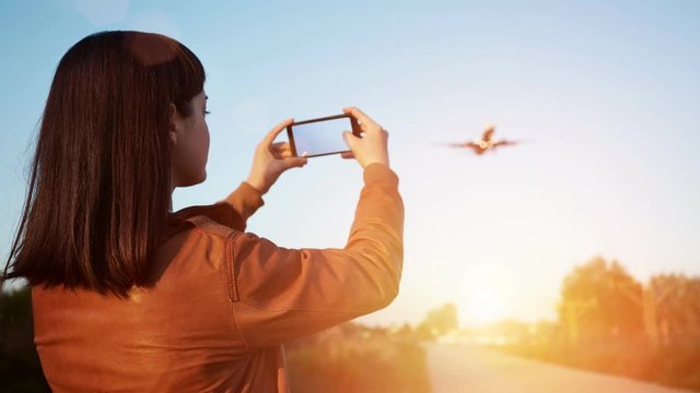 Cinemagraph loop Brunette girl in leather jacket takes video of big airplanes flying over her before landing in airport, on her smart phone at sunrise morning