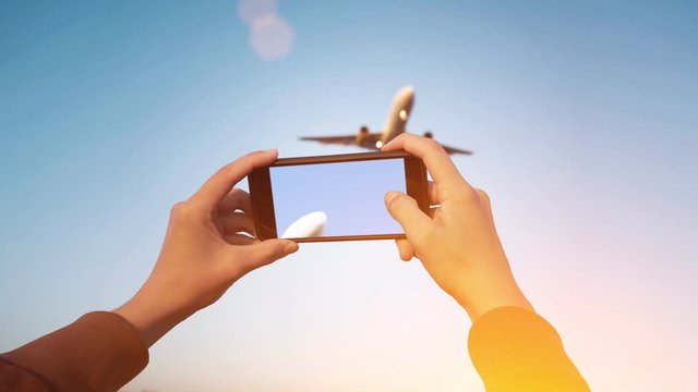 Cinemagraph of spotter girl hands holding smart phone and taking video of big airplanes flying over her head, isolated on clean blue sky background and with dramatic light leaks flares