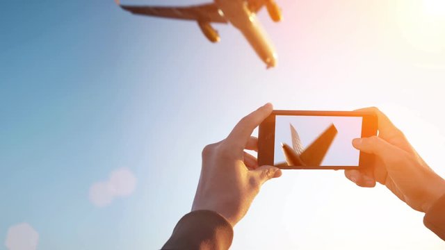 Cinemagraph of spotter girl hands isolated on side holding smart phone and taking video of big airplanes flying over her head at sunset on sunrise time.
