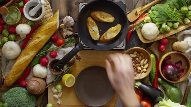 Time lapse of cooking roasted bread with garlic, tomatoes and fresh herbs. Lots of fresh vegetables on wooden table around frying pan