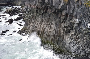 Eine Grosse Welle, welche gegen einen Fels aus Basalt steinen besteht prallt.