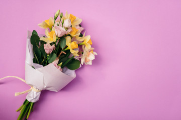A bouquet of daffodils and eustoma on a pink background with an empty space for advertising or text. Top view