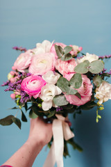 Delicate wedding bouquet of ranunculus flower, freesia and eucalyptus leaves in hand against blue background